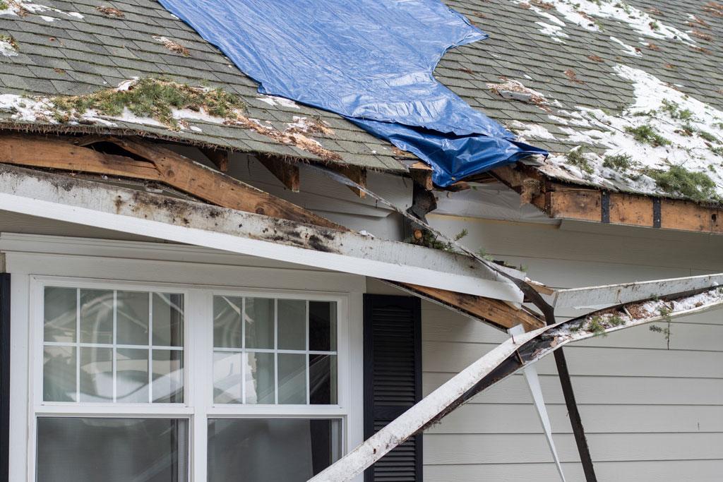 Roof of home damaged by storm. Drain hanging down and tarp over roof hole