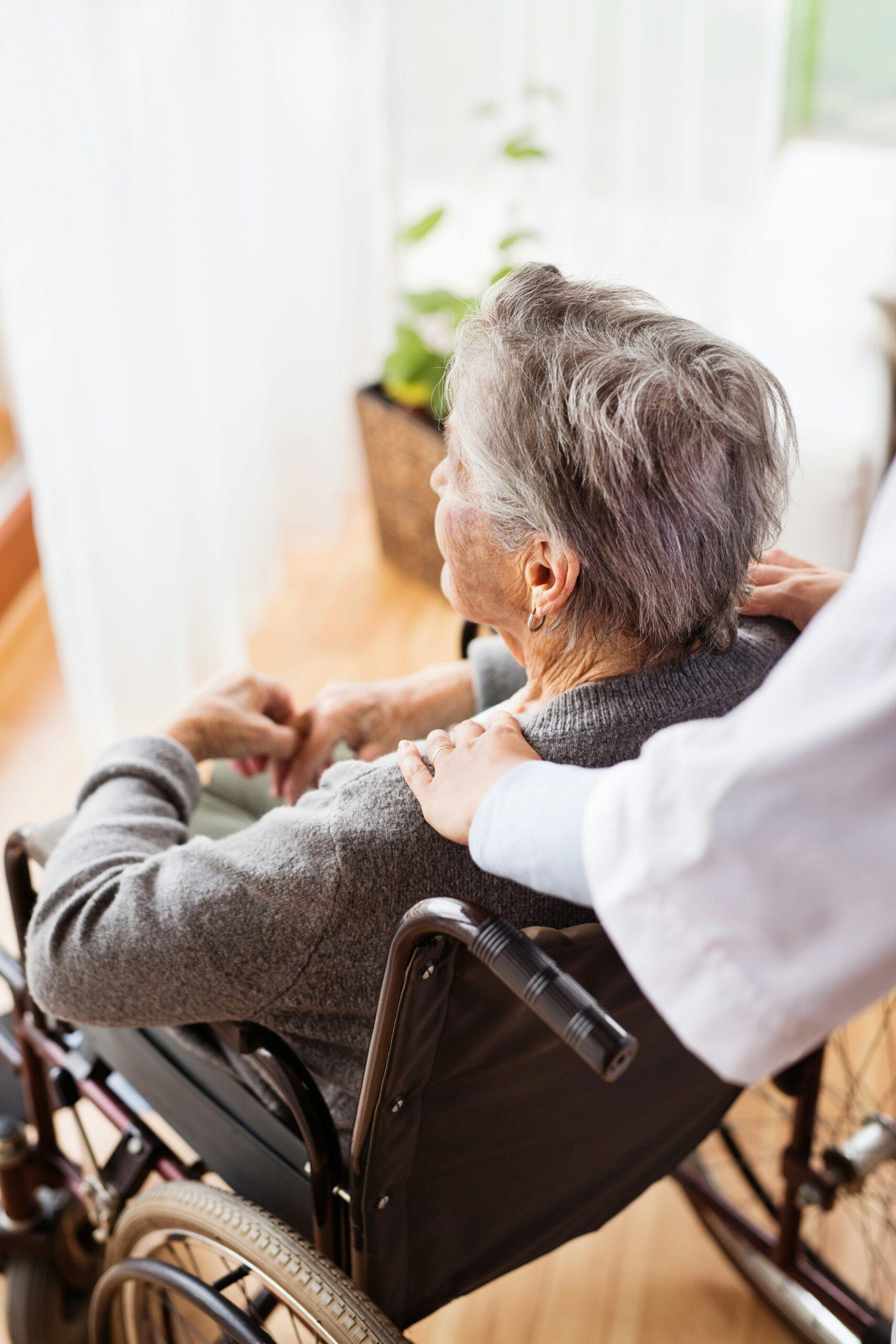 An elderly woman sitting in a wheelchair, looking out the window
